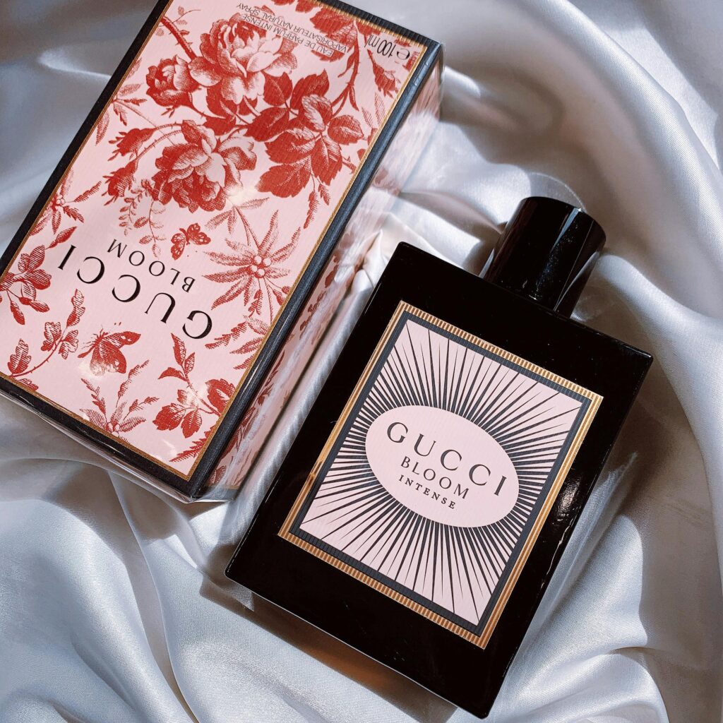 Elegant Gucci Bloom Intense perfume bottle and box on white silk fabric.