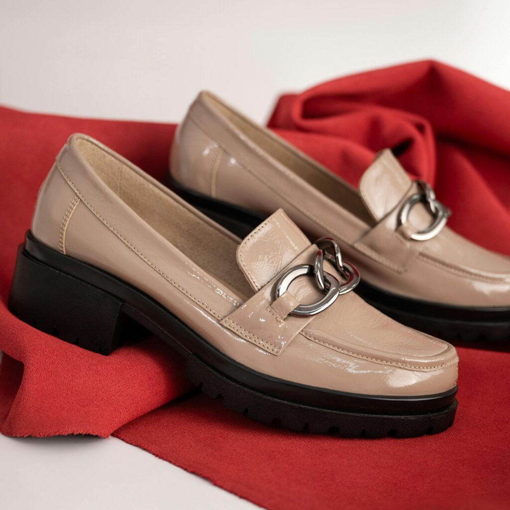 Stylish beige leather women's loafers displayed on a vibrant red fabric background.