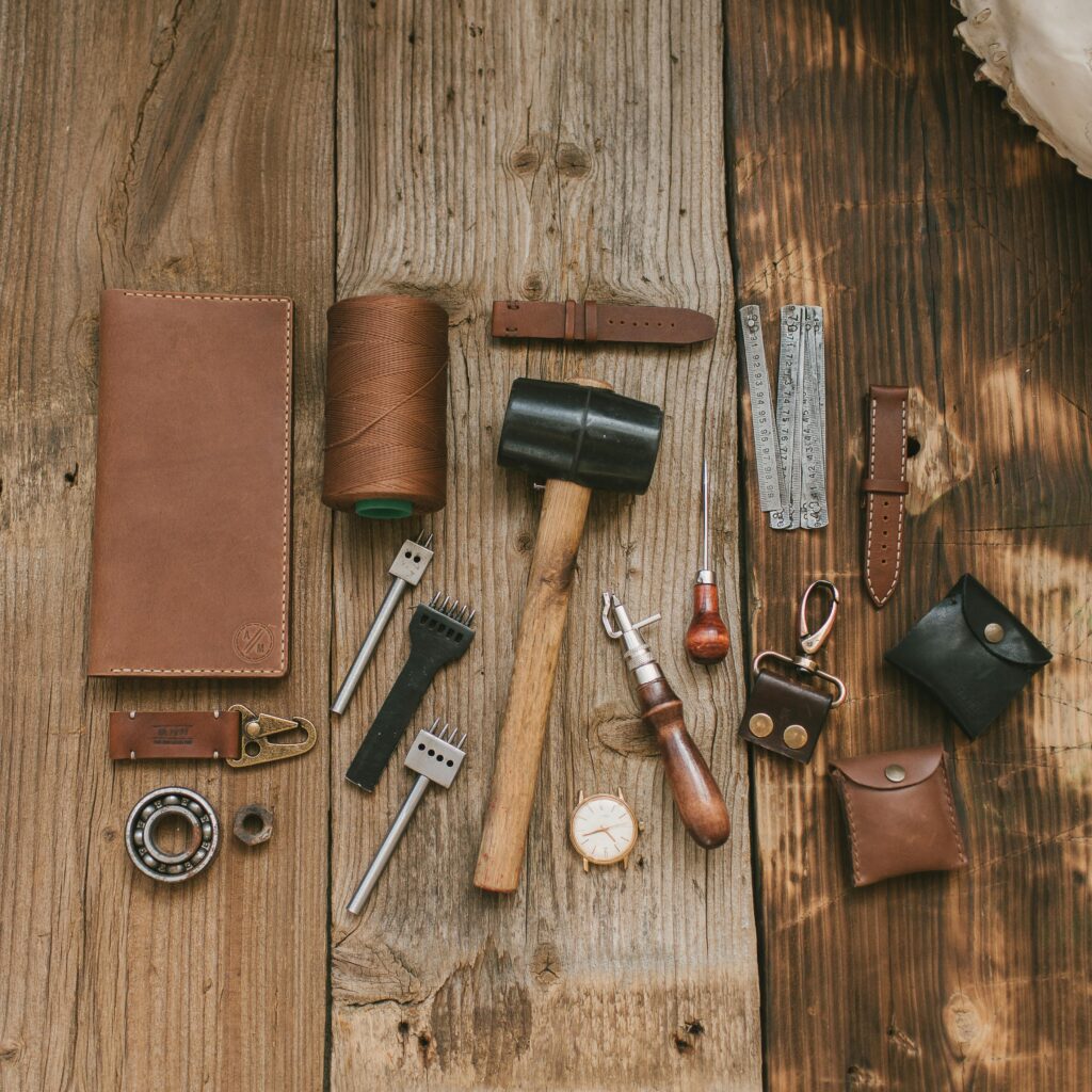 A collection of leather crafting tools and materials arranged on a rustic wooden surface, showcasing artisanal craftsmanship.
